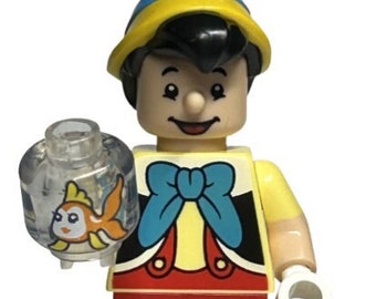 May include: A LEGO minifigure of Pinocchio from Disney's Pinocchio. He is wearing a yellow shirt, red pants, and a blue bow tie. He is holding a clear plastic fishbowl with a goldfish inside. The minifigure is standing on a black LEGO base.