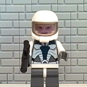 May include: A white Lego minifigure with a white helmet and a black blaster. The minifigure is wearing a gray and black suit with a white belt. The minifigure is standing on a black base.