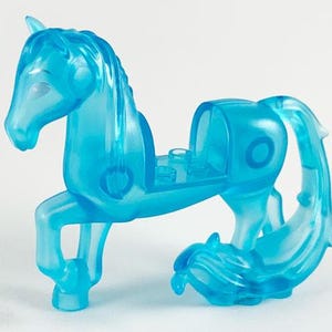 May include: A translucent blue toy horse figurine. The horse has a flowing mane and tail, with a saddle area and a stylized design. The toy is made of a clear, light blue plastic material.