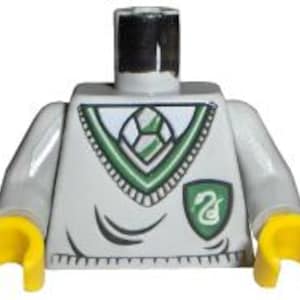 Puede incluir: Un torso de Lego gris claro con manos amarillas. El torso presenta un diseño verde y blanco en la parte delantera, que incluye un escudo con un emblema de serpiente. La figura tiene una parte superior negra.