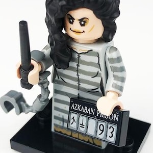 May include: A Lego figure of a character with black curly hair, wearing a gray and white striped prison uniform. The figure holds a black wand and a sign that reads "AZKABAN PRISON" with the number "93".
