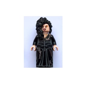 May include: A black LEGO minifigure of a woman with long black hair, wearing a black dress with silver detailing. The minifigure has a dark complexion and a red mouth.