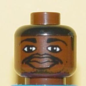 Puede incluir: Primer plano de una cabeza de figura Lego marrón con cabello negro, cejas y bigote. La figura tiene ojos blancos y una expresión sonriente. La cabeza está unida a un torso azul.