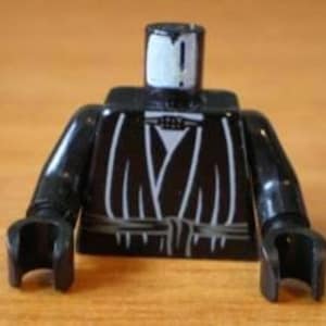 May include: Black Lego minifigure torso with a black robe and a gray belt. The minifigure has a white face with a black mouth and a black belt.