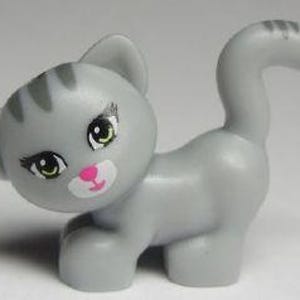 May include: A gray kitten toy with pink nose and green eyes. The kitten is standing on all fours with its tail curled up.