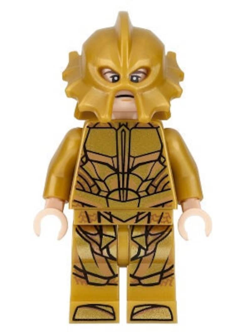 May include: A gold LEGO minifigure of a character wearing a gold helmet with a face mask and a gold suit with a detailed pattern.