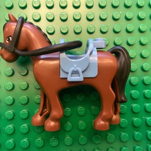 May include: A brown plastic toy horse with a black bridle and a blue saddle. The horse is standing on a green surface.