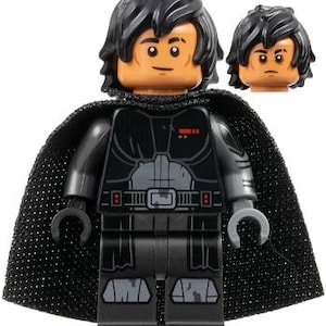 May include: A plastic minifigure featuring a black cape, dark gray torso armor with red accents, and black legs with gray detailing. The figure has black hair and a tan head with a smiling expression, accompanied by an extra head with a serious expression.