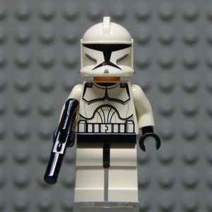May include: A white Lego Star Wars clone trooper minifigure with a black blaster rifle. The figure has a white helmet with a black visor and a black and white chest plate.