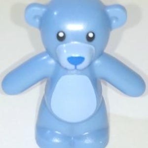 Könnte beinhalten: Eine kleine, glatte, hellblaue Kunststoff-Bärenfigur mit rundem Kopf, zwei Ohren und ausgestreckten Armen. Der Bär hat einen hellblauen ovalen Fleck auf der Brust, eine dunkelblaue Nase und zwei schwarze Augen mit weißen Pupillen, aufrecht stehend.