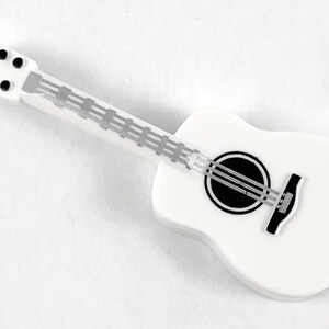 May include: A white miniature acoustic guitar with a black sound hole and bridge. The guitar has a white neck with silver frets and black tuning pegs. The instrument is a decorative item.