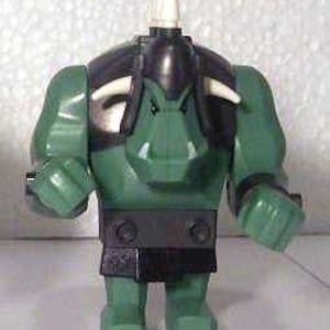Può includere: Una figura Lego verde di una creatura fantasy con un elmo nero, un'armatura per le spalle e una cintura. La figura ha corna bianche e una spina bianca sulla sommità della testa. La figura è in piedi con le braccia lungo i fianchi.