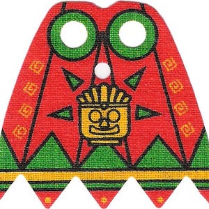 May include: A red fabric cape for a small figure featuring a central yellow stylised face graphic, green circular neck cutouts, and a bottom border with green triangles and a yellow horizontal stripe. The design includes black outlines throughout.