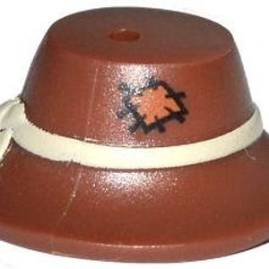 Puede incluir: Un sombrero marrón con una banda blanca y un pequeño parche. El sombrero tiene un ala ancha y una corona cilíndrica. El parche es naranja con costuras negras. El sombrero está hecho de un material brillante.