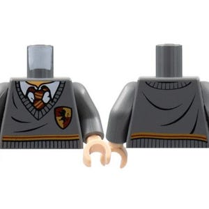 Puede incluir: Un torso Lego gris con manos color canela. La parte delantera del torso presenta un escudo con un león y la parte trasera tiene un diseño a rayas. El torso es parte de un set de Lego de Harry Potter.