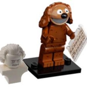 May include: LEGO minifigure of a brown dog with a big smile and a piece of paper in its hand. The figure is standing on a black base. A separate white LEGO minifigure head with a surprised expression is included.
