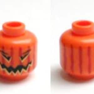May include: Two orange Lego heads, one with a carved jack-o'-lantern face and the other with vertical lines. The jack-o'-lantern face has black eyes and a jagged mouth. The heads are cylindrical with a circular peg on top.
