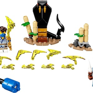 Może przedstawiać: Zestaw Lego Ninjago z czarną kobrą z żółtymi kłami, niebieską minifigurką ninja z żółtą bronią, niebiesko-szara minifigurką węża ze srebrną bronią i kilkoma żółtymi broniami.