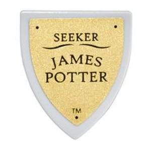 Può includere: Un plettro per chitarra bianco e oro con il testo "SEEKER JAMES POTTER" in nero. Il plettro ha una forma a scudo con un centro dorato e un bordo bianco. Il testo "TM" è in basso.