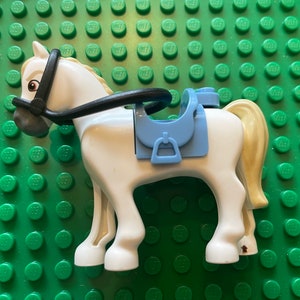 May include: A white plastic toy horse with a black bridle and a blue saddle. The horse has a gold mane and tail.