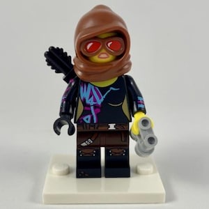 May include: A Lego minifigure of a character wearing a brown hood, red goggles, and a black and purple top. The figure holds a bow and a gray double-barreled gun. The figure stands on a white base.