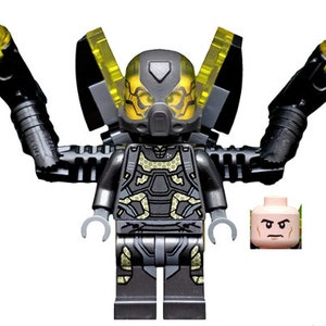 May include: A black and yellow LEGO minifigure of Ant-Man wearing a helmet and a suit with a honeycomb pattern. The minifigure has two yellow blasters attached to its arms.