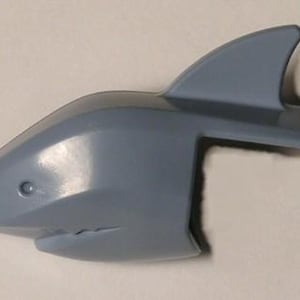 May include: A light blue plastic shark head with a dorsal fin and a small eye detail. The shark's mouth has several small teeth. This toy is likely a building block or part of a larger set.