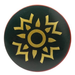 May include: A round, dark green button with a gold sunburst design. The button has a red border and a white background. The sunburst design is centered on the button.