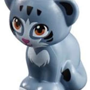 Puede incluir: Una figurita de gato gris y blanco con marcas negras y ojos naranjas. El gato está sentado con las patas metidas debajo del cuerpo.