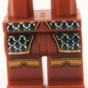 May include: A pair of brown Lego minifigure legs with detailed printing. The design includes green and white scale patterns on the front and gold accents. The legs are a standard size for Lego figures.