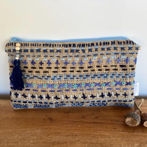 May include: A blue and brown embroidered zippered pouch with a tassel. The pouch is made of a woven fabric with a geometric pattern.