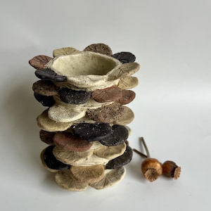 May include: A ceramic vase made of stacked flower-shaped pieces in shades of brown, black, and white. The vase is decorated with a textured surface.