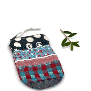 Può includere: Una piccola borsa fatta a mano con un design patchwork. La borsa è realizzata con diversi tessuti, tra cui pois neri e bianchi, stampa floreale, scozzese rosso e blu e denim. La borsa ha una chiusura con coulisse bianca.