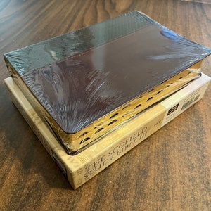 May include: A brown leather-bound book with gold accents and a gold-embossed title: "The Scofield Study Bible NIV".