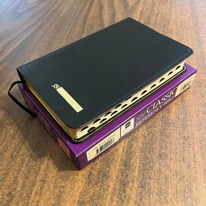 May include: A black leather-bound NIV Classic Reference Bible with gold accents and a gold embossed title on the front cover.