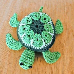 May include: A crocheted turtle toy, predominantly green with a darker green central pattern and lighter green shell. The turtle features four flippers and a small head, all in green yarn. The shell has white detailing.