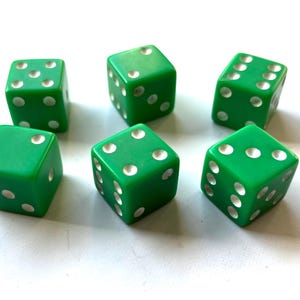 May include: Six green dice with white dots on each side. The dice are arranged in a circle on a white surface.