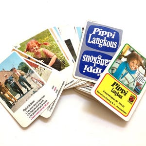 Op de afbeelding: Een verzameling vintage Pippi Langkous speelkaarten. De kaarten bevatten illustraties van Pippi en andere personages, met tekst in het Nederlands. De kaarten zijn gerangschikt op een wit oppervlak.