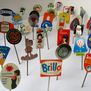 Puede incluir: Una colecci&oacute;n de pines publicitarios vintage que representan diversas marcas y productos. Los pines son coloridos y presentan una variedad de dise&ntilde;os, incluyendo ilustraciones, logotipos y texto. Algunas de las marcas que se muestran incluyen "Crackfree", "Karpeton", "Primula", "Hit Parade", "Didas", "Croma" y "Kolibri Koffie".