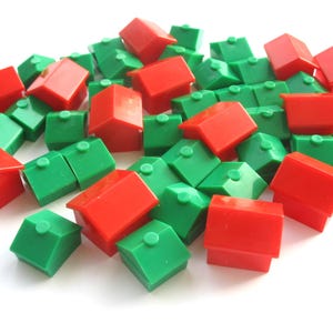 Op de afbeelding: Een verzameling kleine plastic huisvormige spelstukken in levendige rode en groene kleuren. Elk stuk heeft een eenvoudig ontwerp met een zadeldak en een kleine schoorsteen op de top, verspreid in een losse hoop op een witte ondergrond.