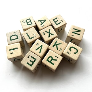 May include: A collection of wooden Scrabble tiles with green letters and numbers. The letters include A, B, C, D, E, K, L, N, R, V, and X. The tiles are scattered on a white surface.