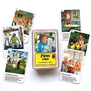 Op de afbeelding: Een vintage Pippi Langkous kaartspel. Het spel bevat een doorzichtige plastic doos met een kaart met Pippi, en verschillende andere kaarten met afbeeldingen van Pippi en haar vrienden. De kaarten zijn wit met kleurrijke illustraties.