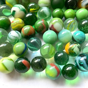 May include: A collection of green, white, and multi-colored glass marbles. The marbles are arranged in a random pattern on a white surface.