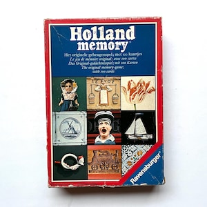 Peut inclure: Boîte de jeu vintage "Holland Memory" avec une bordure rouge et un fond bleu. La boîte présente le titre du jeu et diverses images sur le thème néerlandais, dont une poupée, une tulipe et un moulin à vent. Fabriqué par Ravensburger.