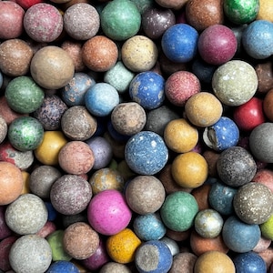 May include: A large collection of spherical glass marbles in a variety of colours including blue, green, yellow, pink, and brown. The marbles feature diverse textures, ranging from smooth and glossy surfaces to matte, weathered, and speckled finishes.