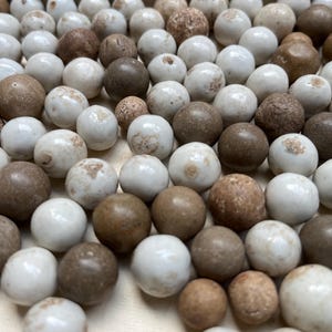May include: A close-up of a collection of marbles in shades of brown and white. The marbles have a smooth, glossy finish and vary in size. Some have speckled patterns, others are solid in colour.