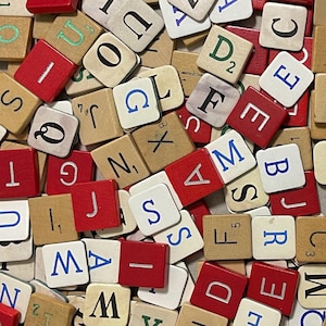 Pode incluir: Uma coleção de peças de jogo quadradas de madeira espalhadas em uma pilha. As peças apresentam letras e números impressos em preto, azul ou verde, algumas com acabamento em madeira natural e outras pintadas em vermelho sólido.