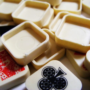 Pode incluir: Pe&ccedil;as de jogo e bandejas quadradas de cor marfim espalhadas. As pe&ccedil;as do jogo apresentam naipes e n&uacute;meros de cartas de jogar em vermelho e preto. As bandejas t&ecirc;m formato quadrado com cantos arredondados.