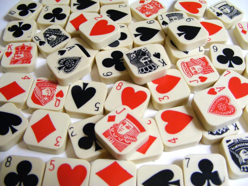 Pode incluir: Uma cole&ccedil;&atilde;o de azulejos quadrados brancos sujos com naipes e valores de cartas de jogar. Os azulejos exibem cora&ccedil;&otilde;es vermelhos, espadas pretas, paus e ouros, juntamente com figuras e n&uacute;meros. A disposi&ccedil;&atilde;o cria um padr&atilde;o visualmente envolvente.