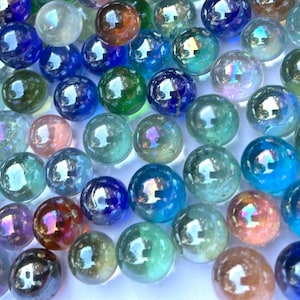 Può includere: Una collezione di biglie di vetro iridescenti in vari colori, tra cui blu, verde e arancione. Le biglie hanno una superficie riflettente e lucida, creando un'esposizione giocosa e colorata. Queste biglie sono adatte per giochi o scopi decorativi.